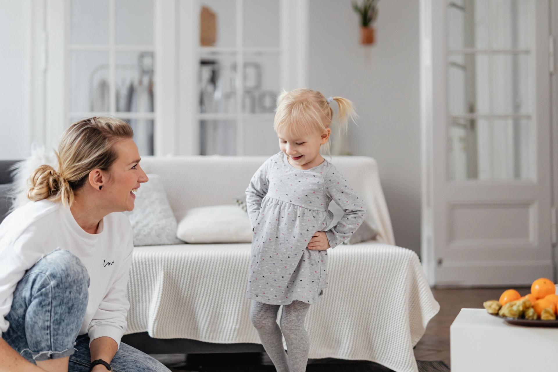 A mother and her young daughter laughing together in a bright, tidy living room