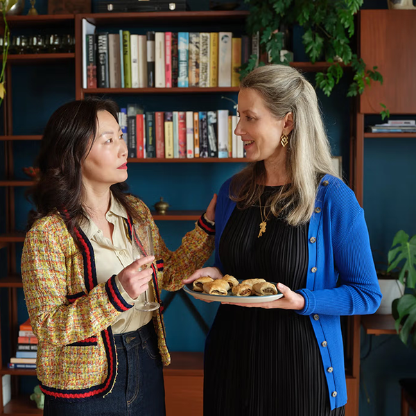 Two women chatting, one holding a champagne flute and the other a plate of pastries.