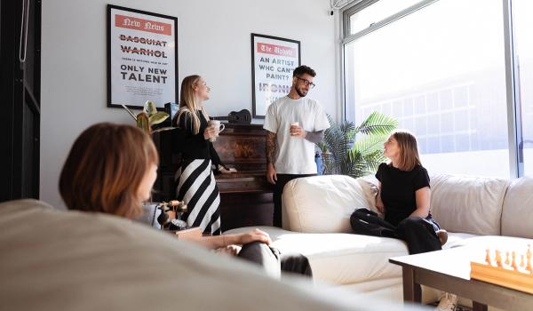 Four adults socialize in a bright, modern lounge featuring art posters and a chessboard.