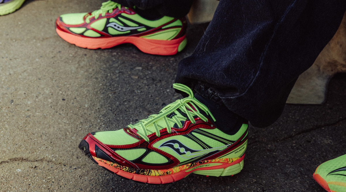 Two pairs of bright green, red, and orange Saucony running shoes on dark pavement.