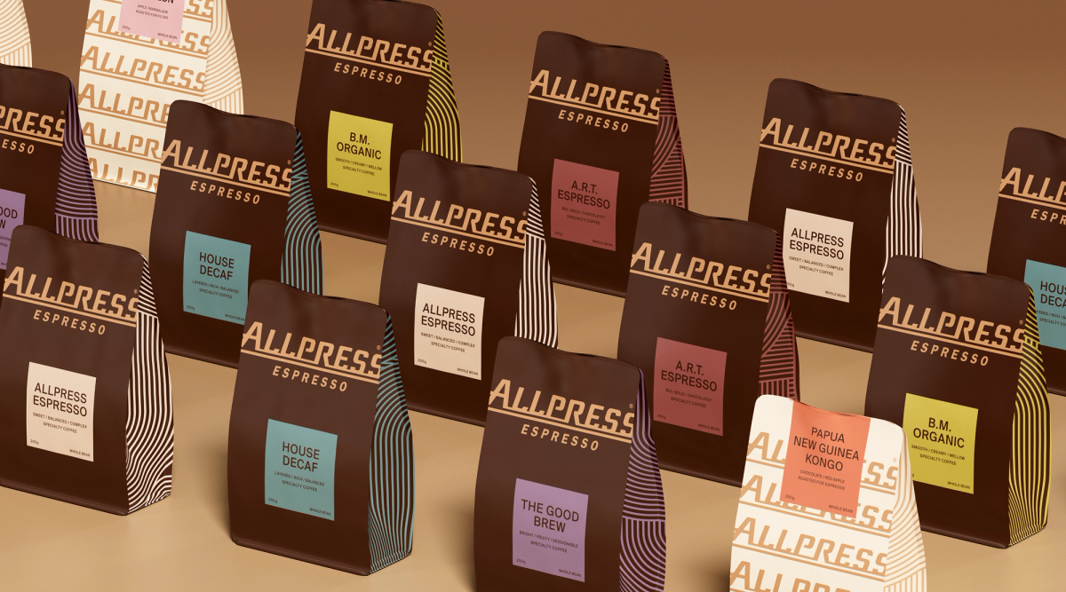 An array of Allpress Espresso coffee bags, primarily dark brown with colorful labels and striped sides, along with one white bag.
