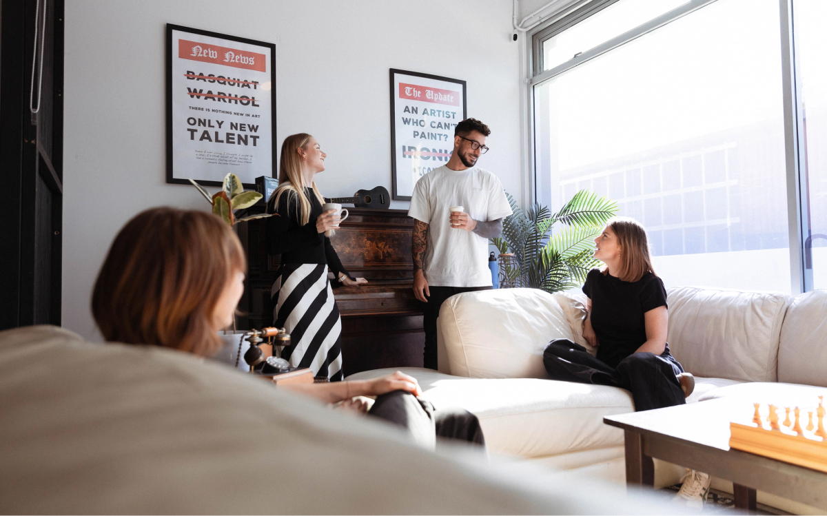 Four people chatting casually in a bright, modern living room with a white sofa.