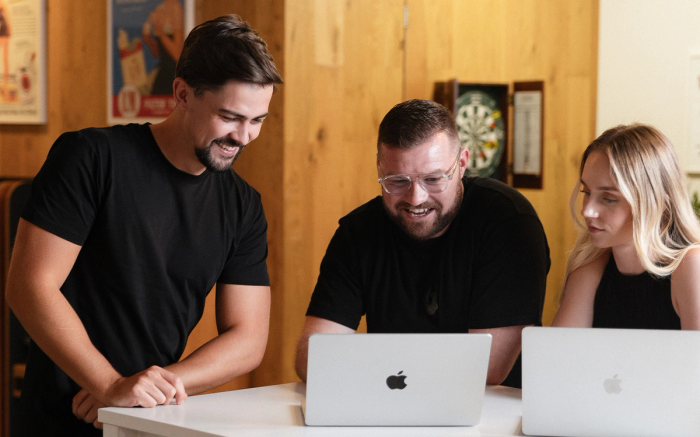 Three people smiling while working on laptops.