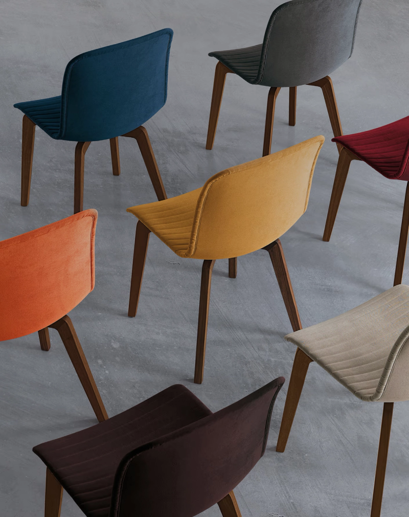 Modern upholstered chairs in teal, grey, yellow, red, orange, brown, and beige, on a grey floor.
