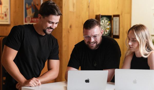 Three smiling colleagues collaborating on laptops.