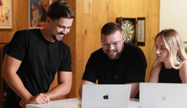 Three smiling colleagues collaborating on laptops.