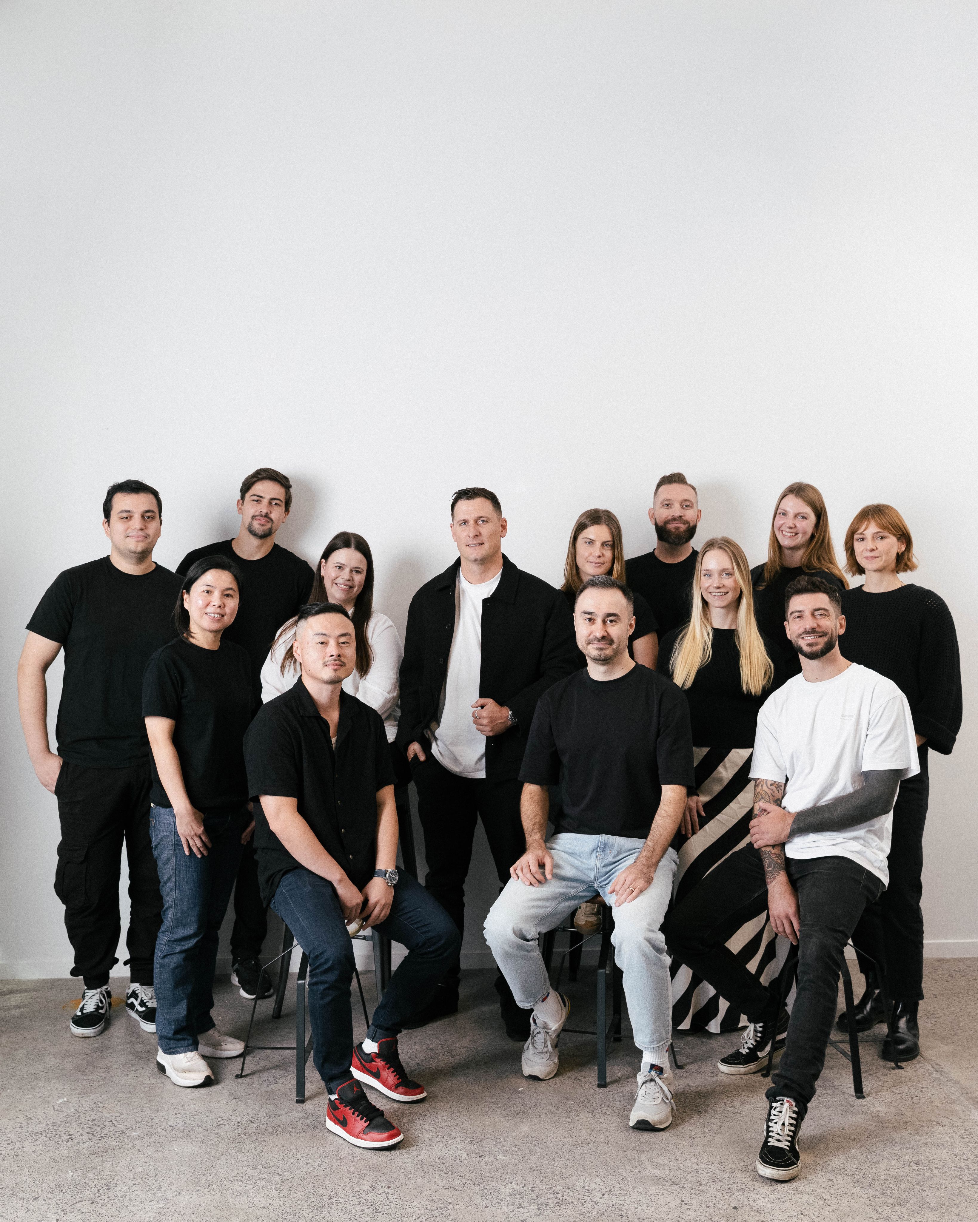 A diverse team of 15 people smiling and posing against a white background.