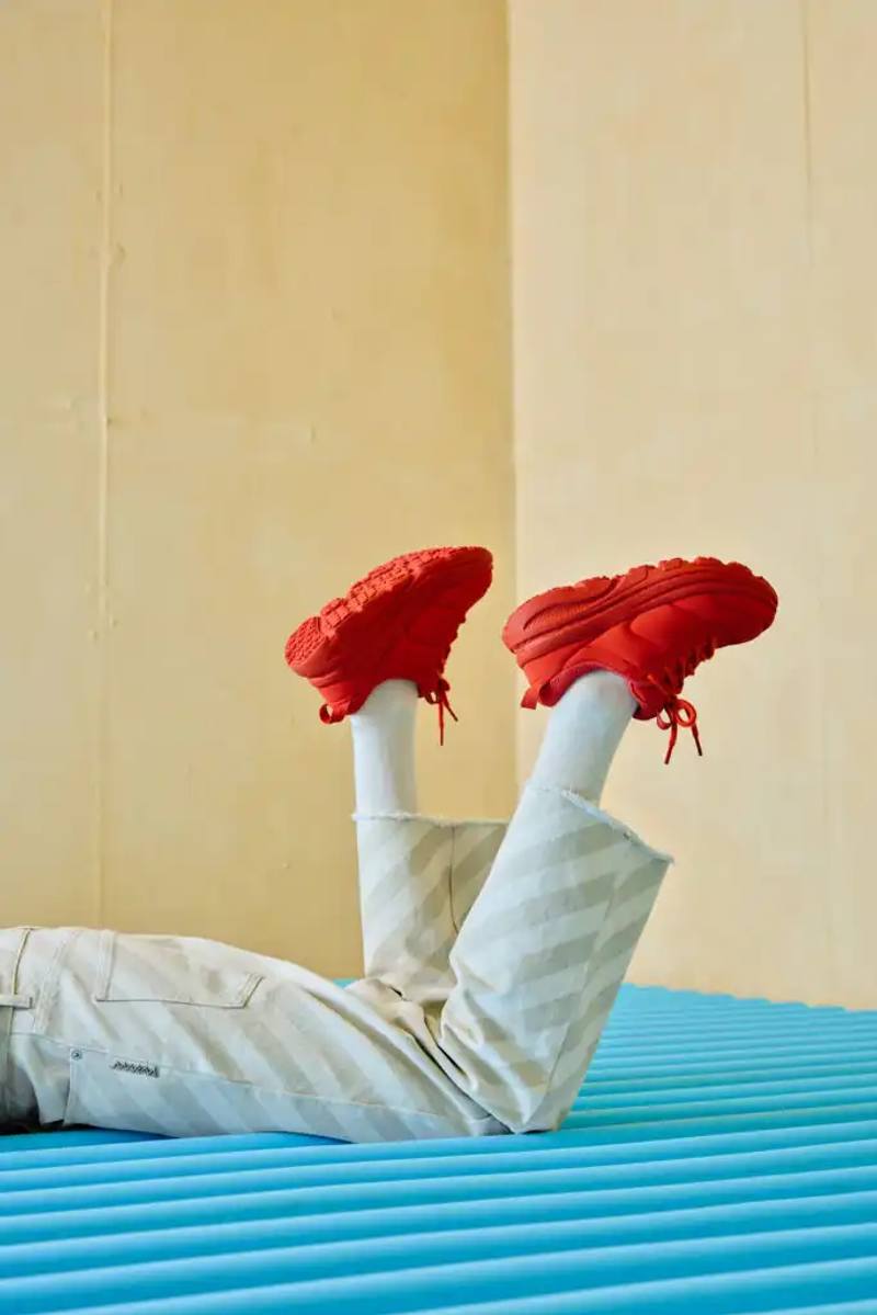 photo of the collaboration between athletic footwear brand Hoka and fashion label Marni on their new Bondi B3LS sneaker. It details the shoe's technical features including a cushioned sole, mesh upper with TPU reinforcements, and rubber outsole with traction lugs. The piece describes the sneaker's four color options (red, beige, blue, brown) and three interchangeable lace styles. The article also reports on the Milan launch event at Villa Clea featuring foam installations by Finemateria, performances by artist Marta Del Grandi and dancers Federica D'Aversa and Rafael Candela, plus a multisensory dining experience by Mimosa Milano. The sneakers are available for €395 on both brands' websites.