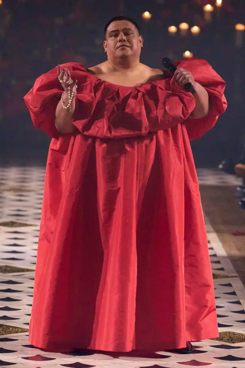 A diverse runway scene featuring models of various ages, body types, and backgrounds wearing Willy Chavarria's Fall 2025 "Tarantula" collection. The designs showcase rose-adorned blazers, Western-inspired hats, and a rich color palette of gold, blue, crimson, and plum against the backdrop of The American Cathedral in Paris.