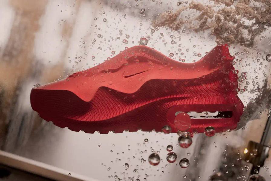 The Nike Air Max 1000 features a vibrant red, 3D-printed upper with a mix of smooth and textured surfaces. The heel showcases a clear Air unit, highlighting the shoe's innovative cushioning technology.