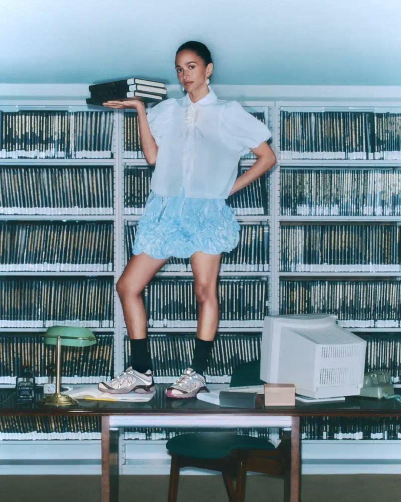 Three Gohar sisters—Laila, Nadia, and Janna—seated in a New York library wearing SALOMON XT-Whisper sneakers. They're arranged in stylish poses among bookshelves, demonstrating the shoe's elegant design in a quiet setting that reflects the "whisper" concept.