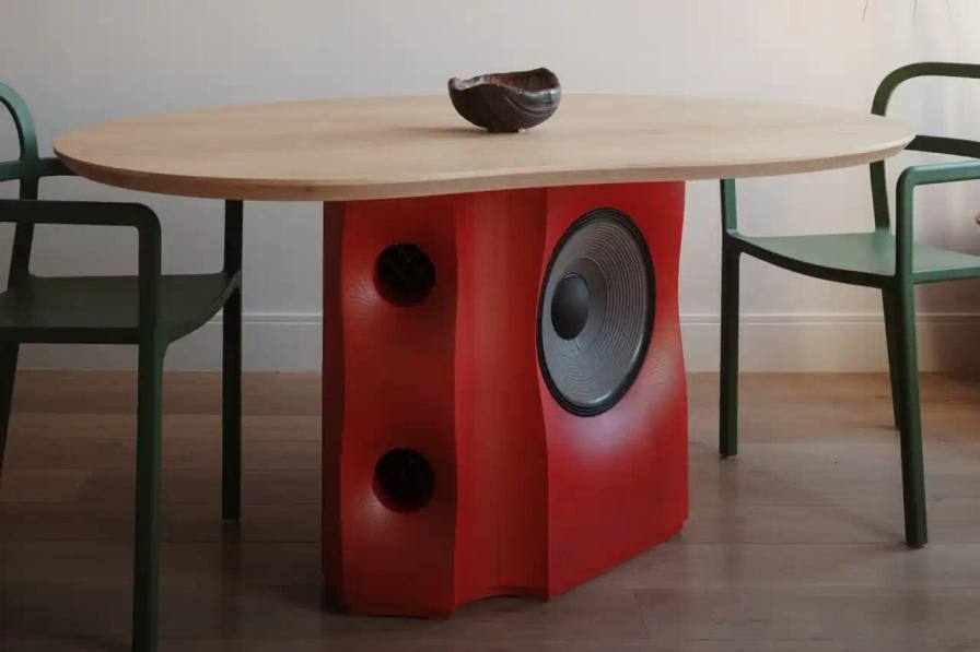 Joel Seigle The Table Bass dining table by Joel Seigle combines a JBL subwoofer in an iridescent red leg with solid ash wood, perfect for space-constrained urban homes.