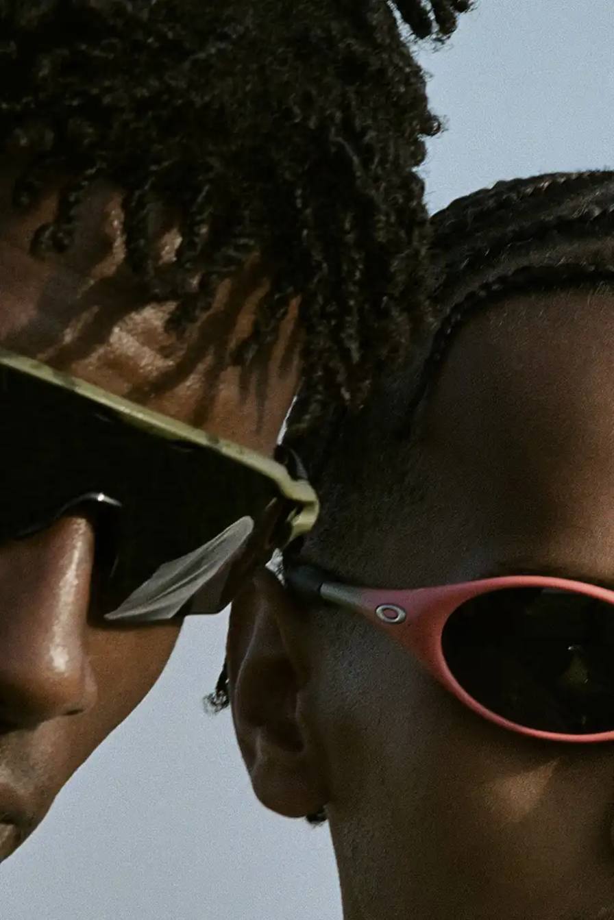 The collection includes a variety of products, such as sunglasses in gradient green and red colorways with metallic Oakley branding, washed-out black denim jackets and bottoms with distressed details, printed tops showcasing blurred rave scenes, and a classic brown leather slip-on sneaker.