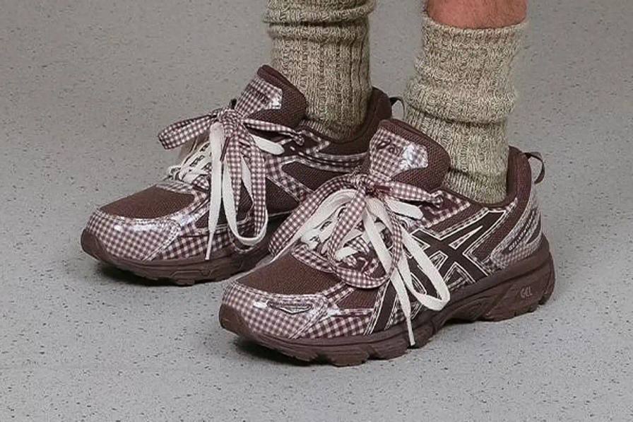 photo of the collaboration between sustainable fashion brand STORY mfg. and ASICS on the GEL-VENTURE 6 sneaker. It details the two gingham colorways ("Reddish Brown" and "Vanilla Violet Quartz"), the unique woven lacing system inspired by Baghdad skaters, and pricing ($133 USD). The article also describes the two-day launch event at The Truman Brewery in London on April 18-19, where visitors can contribute embroidery to a community art project while enjoying refreshments. The article provides purchase information and explains STORY mfg.'s sustainable fashion background.