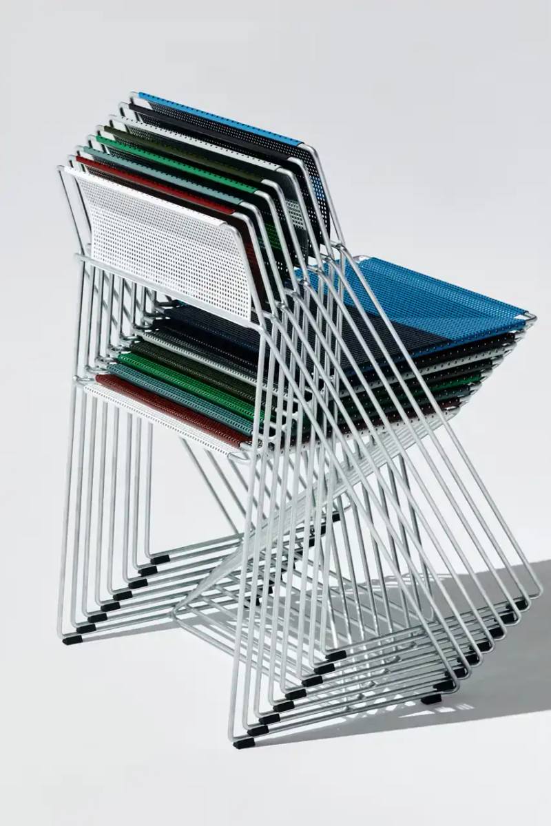 The X-Line Chair by Niels Jorgen Haugesen features a minimalist steel frame with perforated seat and distinctive X-shaped stacking design.