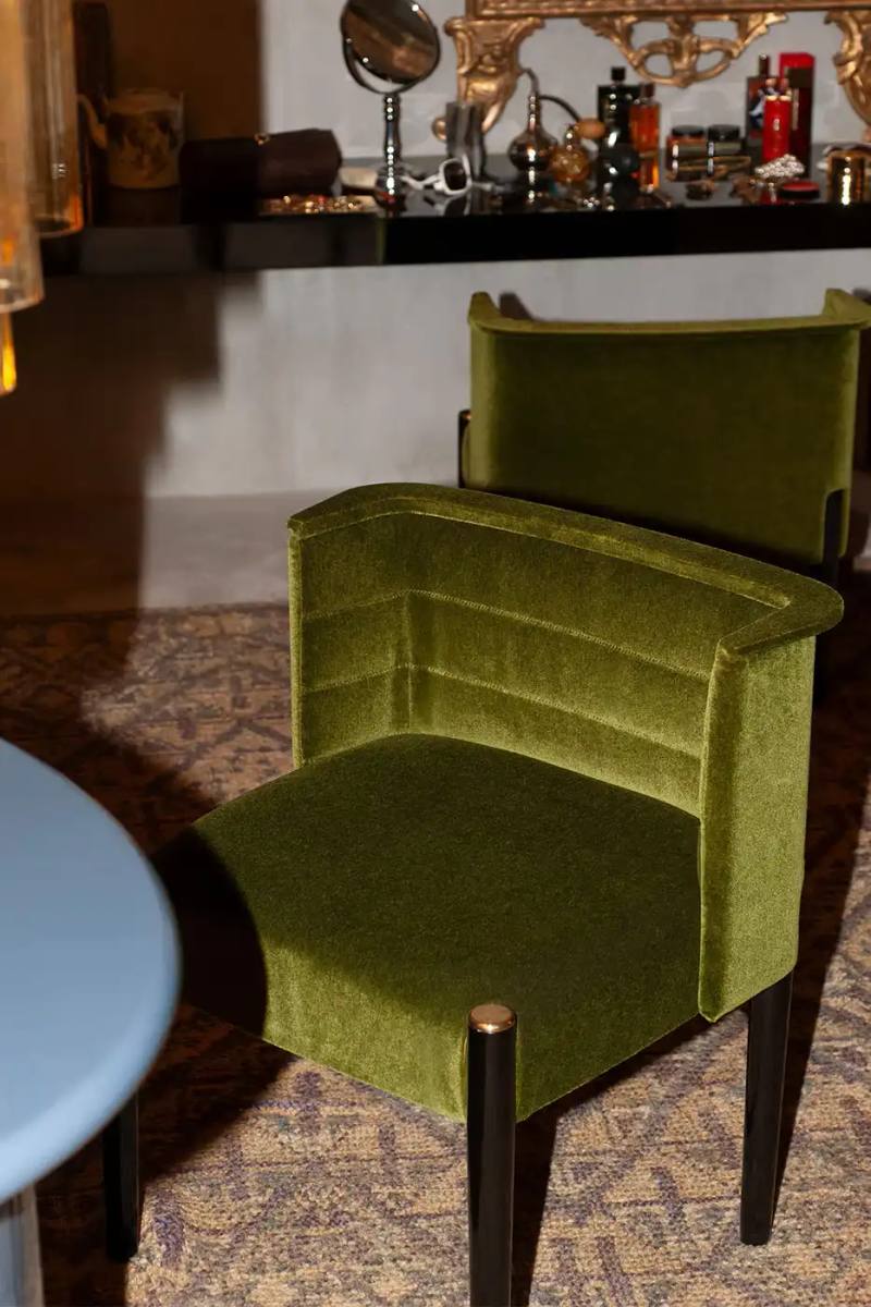 photo of design collaboration between Loro Piana and Dimoremilano at Milan Design Week 2025. The installation, named "La Prima Notte di Quiete," features a cinema-inspired interior design experience with multiple rooms decorated in 1970s-80s style. The spaces showcase new furniture pieces upholstered in Loro Piana fabrics, including dining tables, poufs, cabinets, beds, and armchairs. The immersive experience includes ambient sound design and can be visited at Loro Piana's Milan headquarters until April 13, with reservations available through their booking platform.