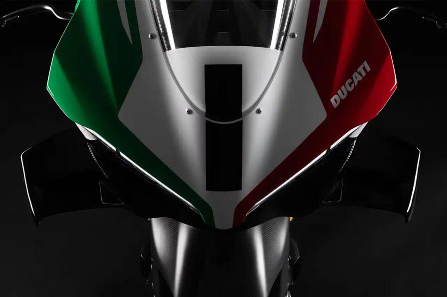 Ducati A side profile view of the Ducati Panigale V4 Tricolore motorcycle, showcasing its sleek racing design with asymmetrical Italian flag-inspired color scheme. The bike features carbon fiber rims, a racing-inspired silhouette, and a distinctive checkered flag motif, highlighting its special edition status and high-performance engineering.