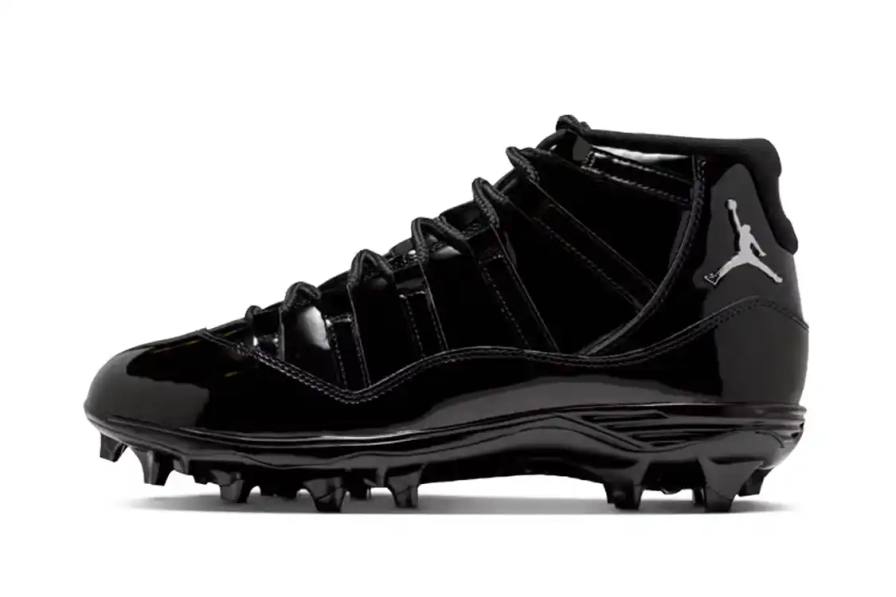 Air Jordan 11 TD football cleats in all-black design with patent leather mudguard, releasing spring 2026 for $225.