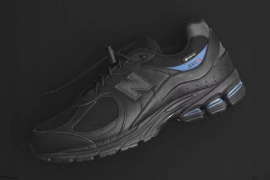 JJJJound x New Balance 2002R GORE-TEX sneaker in all-black colorway, featuring mesh and leather construction with a subtle blue heel accent and GORE-TEX waterproof technology