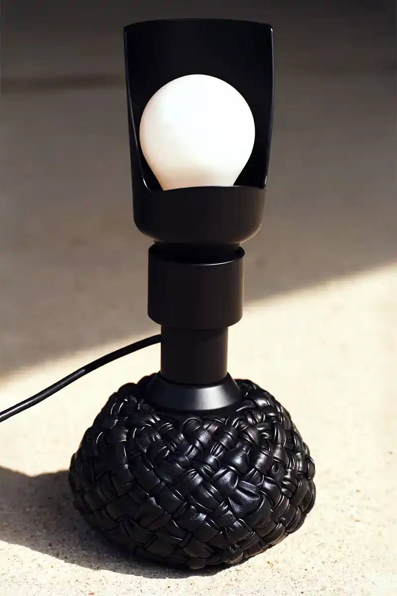 A Bottega Veneta limited edition Flos Model 600 table lamp with a leather base featuring the brand's distinctive Intrecciato woven leather technique. The lamp is shown in a muted green color, with a flexible base that can be positioned at multiple angles.