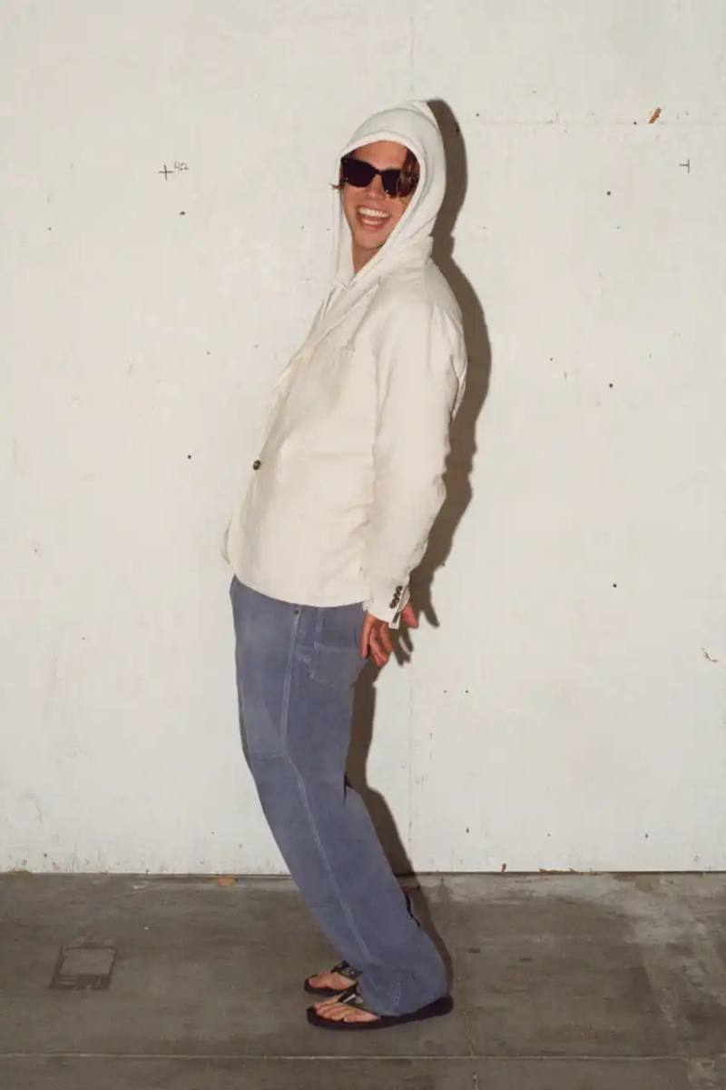 Stüssy Spring 2025 collection lookbook featuring an urban model wearing an oversized camouflage jacket, baggy denim trousers, and wide-cut shorts in muted green and blue tones.
