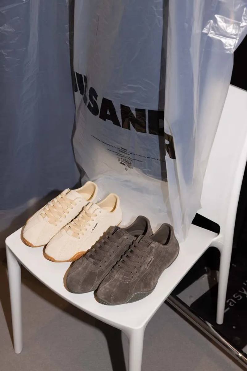 Studio image of Jil Sander and Puma low profile leather sneaker in ivory and dark brown with a thin rubber sole and minimal branding.