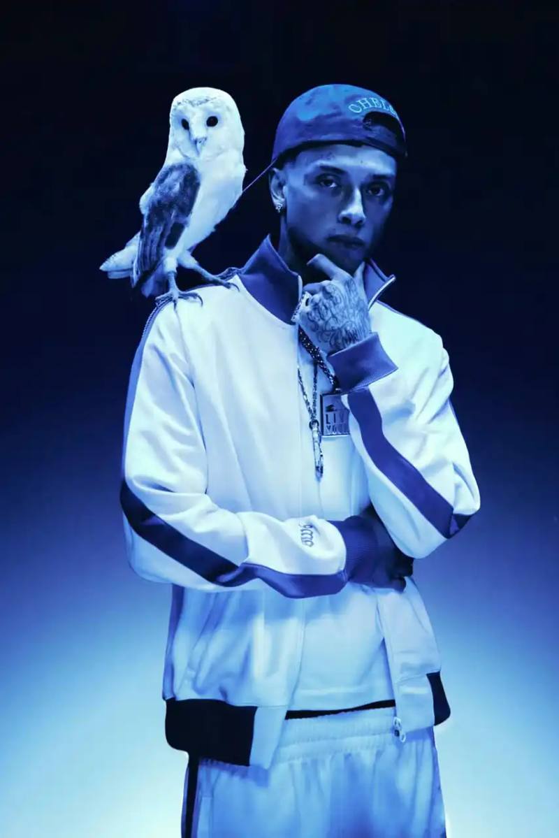 image about October's Very Own and Chelsea Football Club launching a collaborative clothing line. British rapper Central Cee models the collection which includes a varsity jacket, various shirts, hoodie and cap. The partnership combines Toronto streetwear culture with London football heritage through items featuring a merged OVO-Chelsea logo design.