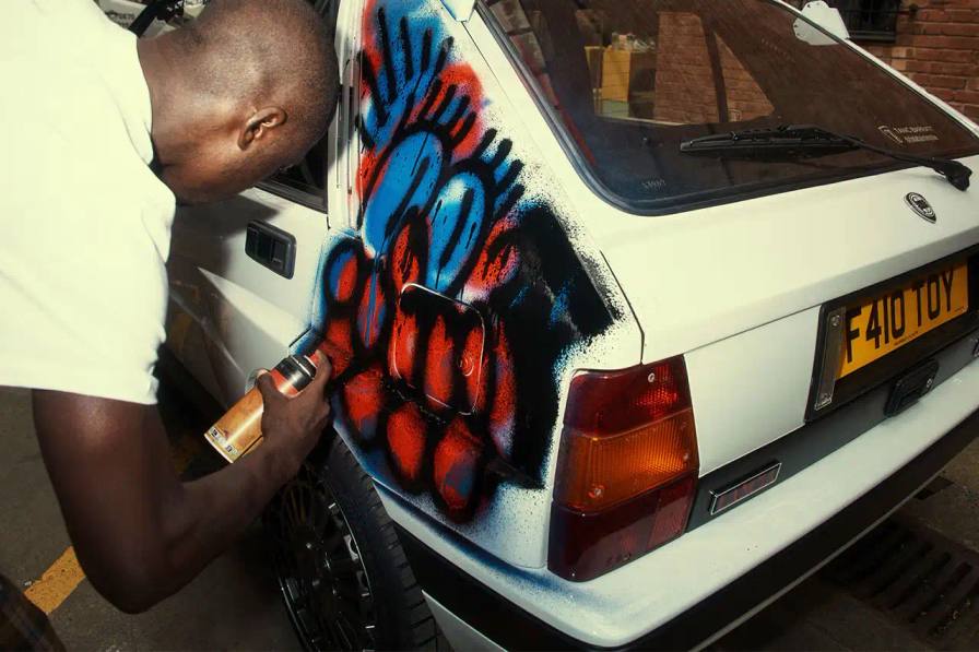 A Lancia Delta Integrale rally car painted by artist Slawn, featuring bold artistic interpretations of the classic Martini racing livery with contemporary street art elements.