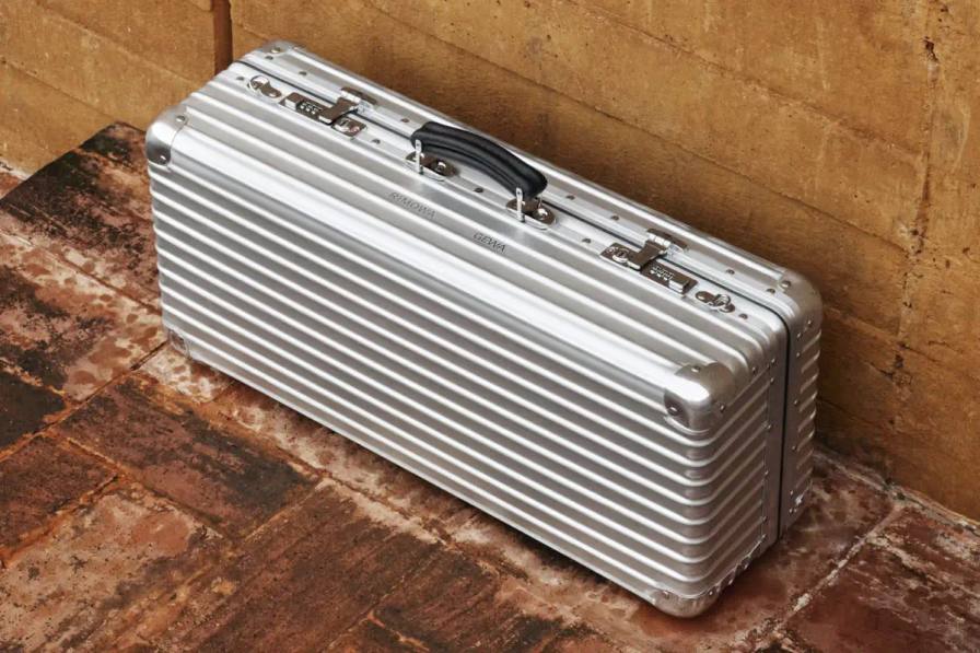 Silver RIMOWA x GEWA aluminum trumpet case with grooved exterior, leather handle, and shoulder strap shown at three-quarter angle