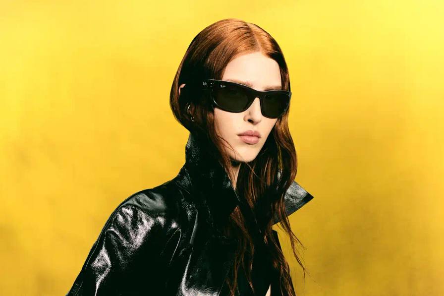 photo of Ray-Ban's updates to two classic eyewear designs. It covers how the 95-year-old company has refreshed the Balorama frame (originally from 1967) with enhanced structural elements while maintaining its distinctive wraparound profile. The article also describes the new Mega Wayfarer variation, which keeps the signature square silhouette but introduces wider temples and thicker rims. The piece mentions Ray-Ban's history of design innovation and cultural relevance, noting how these updated classics honor their original character while incorporating modern features.