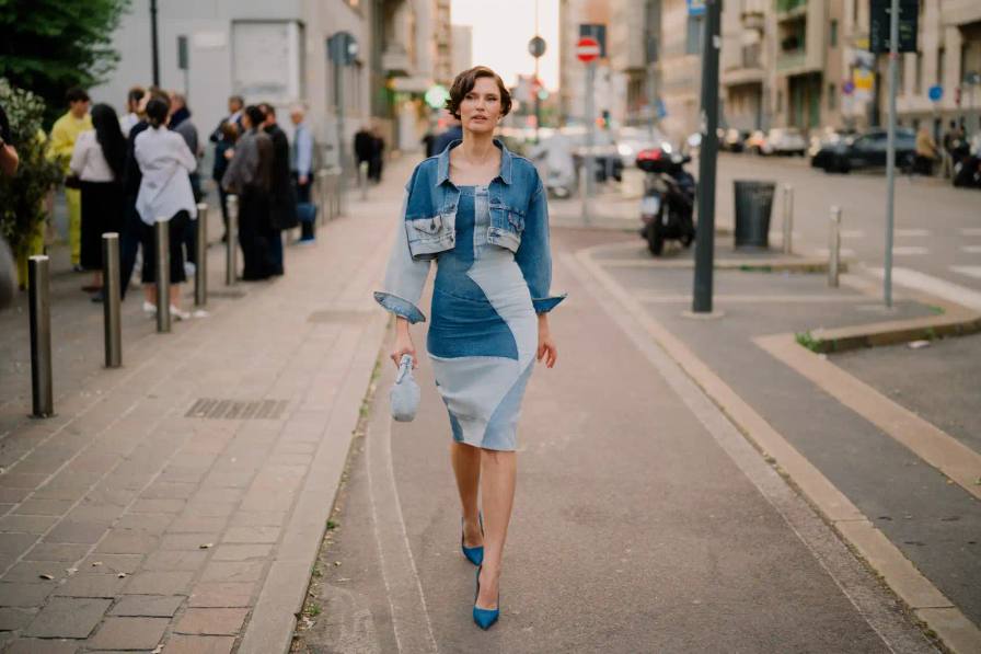 Photograph of Bianca Balti wearing a custom patchwork denim Levi's dress and holding a small denim bag standing in front of a yellow wall with text.