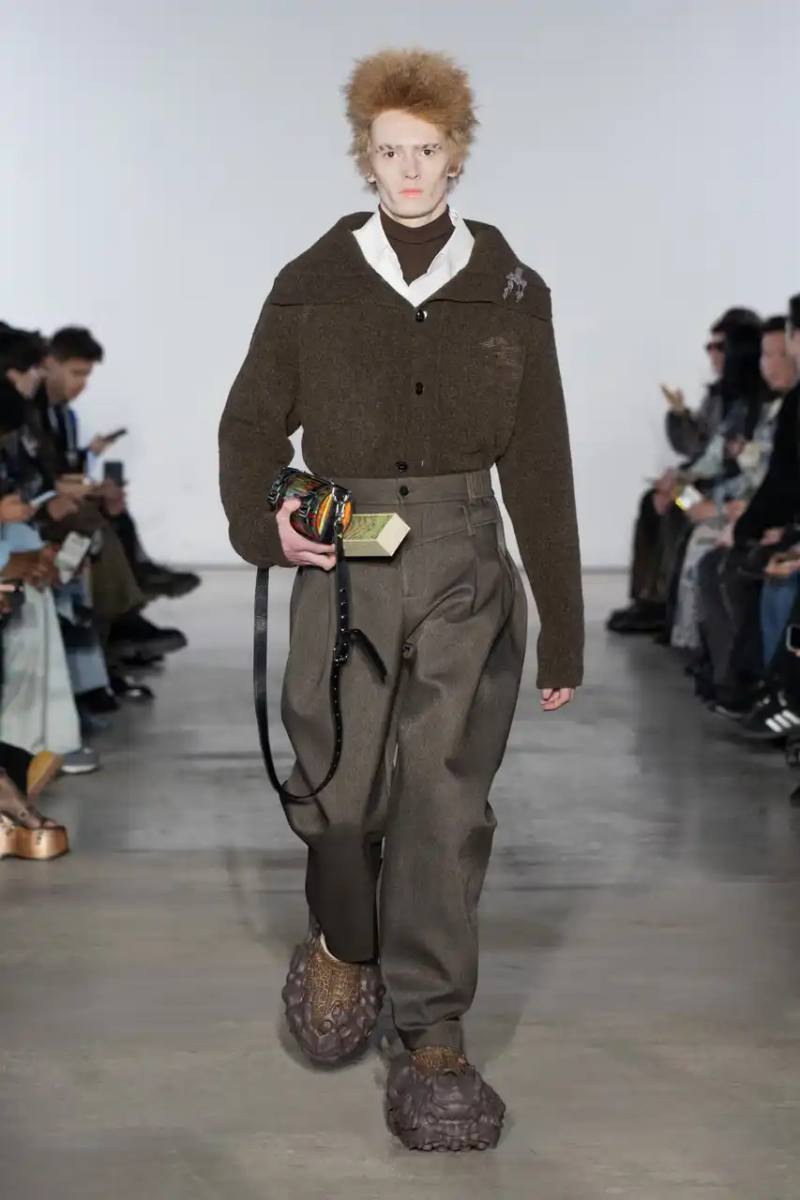 Feng Chen Wang Runway image of a model wearing Feng Chen Wang's Fall/Winter 2025 collection, showcasing oversized ceramic-textured UGG slippers and layered outerwear inspired by mythical Chinese creatures from the Shan Hai Jing text