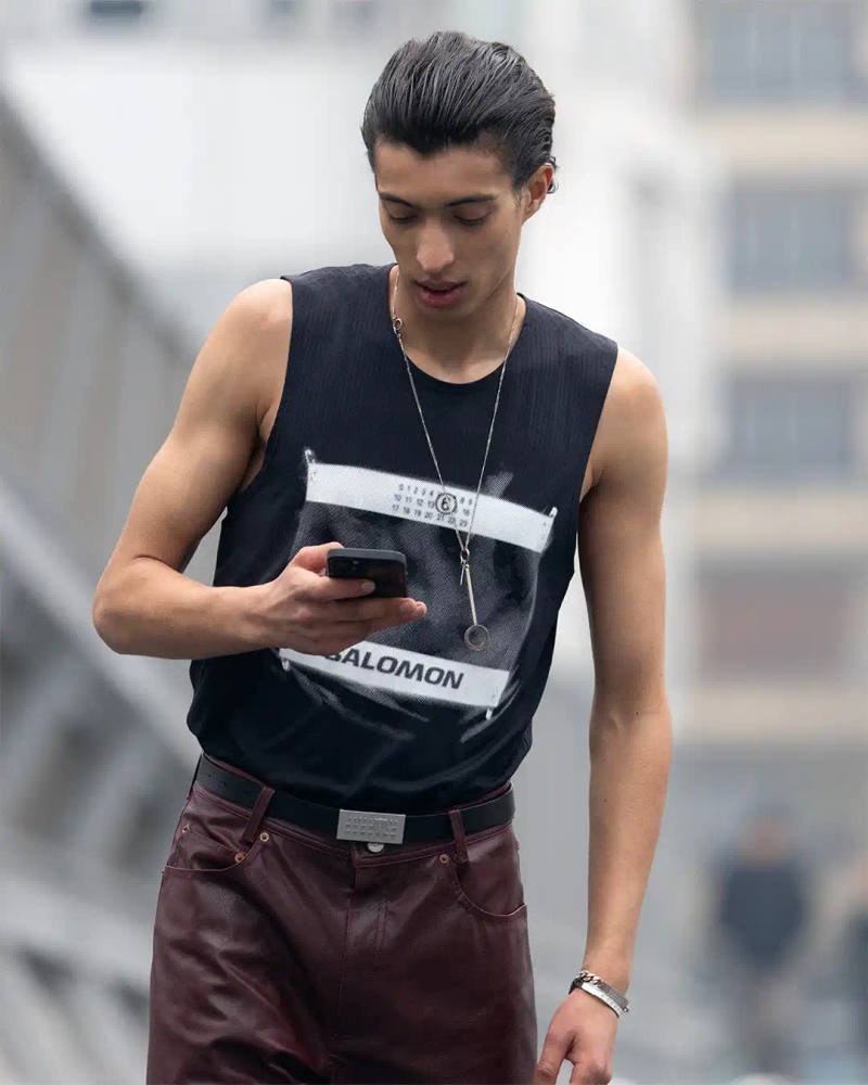 photo of the Spring/Summer 2025 collaboration between fashion brand MM6 Maison Margiela and athletic brand Salomon. It describes their unisex collection that combines experimental design with technical sportswear functionality. The collection includes running-inspired garments with technical materials and distinctive proportions, plus footwear like the Spectur 2 running shoe in black and sage green, and new colorways of the XT-4 Mule. The collection will be released in two drops on April 17 and May 8, available through both brands' websites and select retailers.
