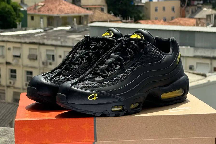 Corteiz x Nike Air Max 95 'Honey Black' sneaker featuring an all-black premium leather upper with contrasting Tour Yellow accents on the branding and Air cushioning units. The sleek design showcases Corteiz branding on the lateral toe, heel, tongue and outsole, with London coordinates visible on the heel. The shoe maintains the Air Max 95's signature layered construction with mesh detailing on the upper.
