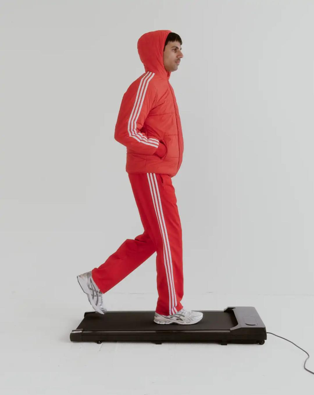 Shai Datauker wearing his daily uniform-a bright red Adidas tracksuit and white t-shirt-sitting in a minimalist interior during an interview about fashion and identity.