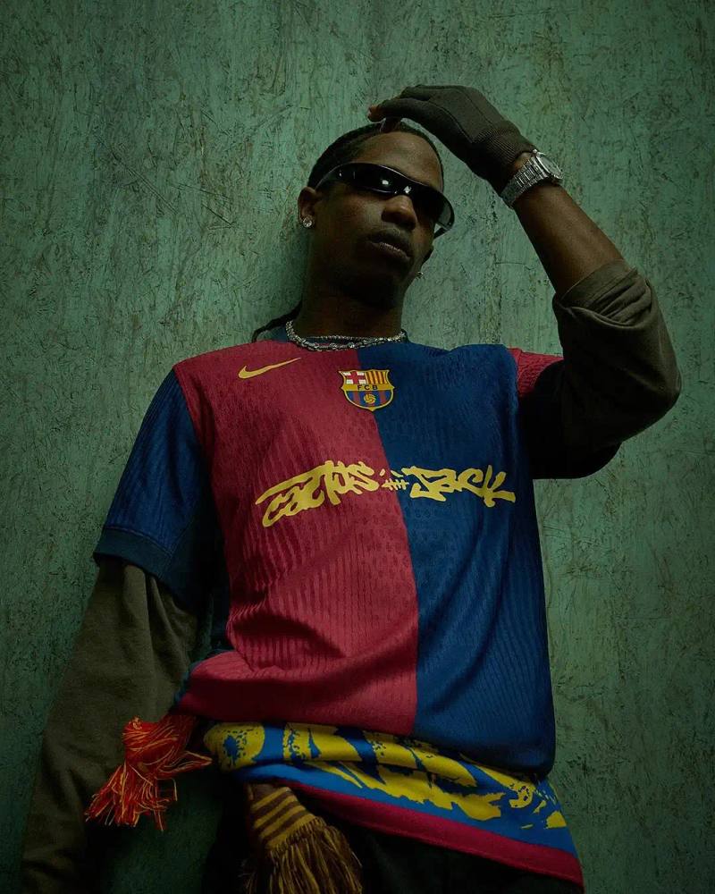 FC BARCELONA AND TRAVIS SCOTT TEAM UP FOR LIMITED COLLECTION image of the collaboration between FC Barcelona and Travis Scott, facilitated by Spotify. It details how the rapper designed a special kit featuring his Cactus Jack logo for the upcoming El Clásico match against Real Madrid on May 11. The article includes a quote from Scott about the partnership and describes the merchandise collection, which includes Nike-branded apparel with vintage-style acid washing. The collection continues Barcelona's tradition of featuring musical artists on special match kits through their Spotify partnership.