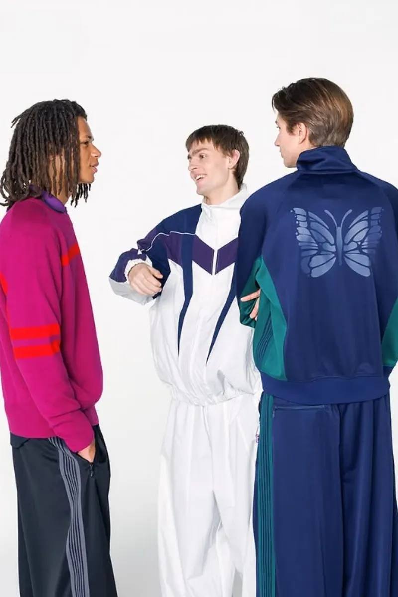Two fashion models present sportswear from the NEEDLES and FILA FW26 collection in teal, navy, and magenta against a neutral studio backdrop.