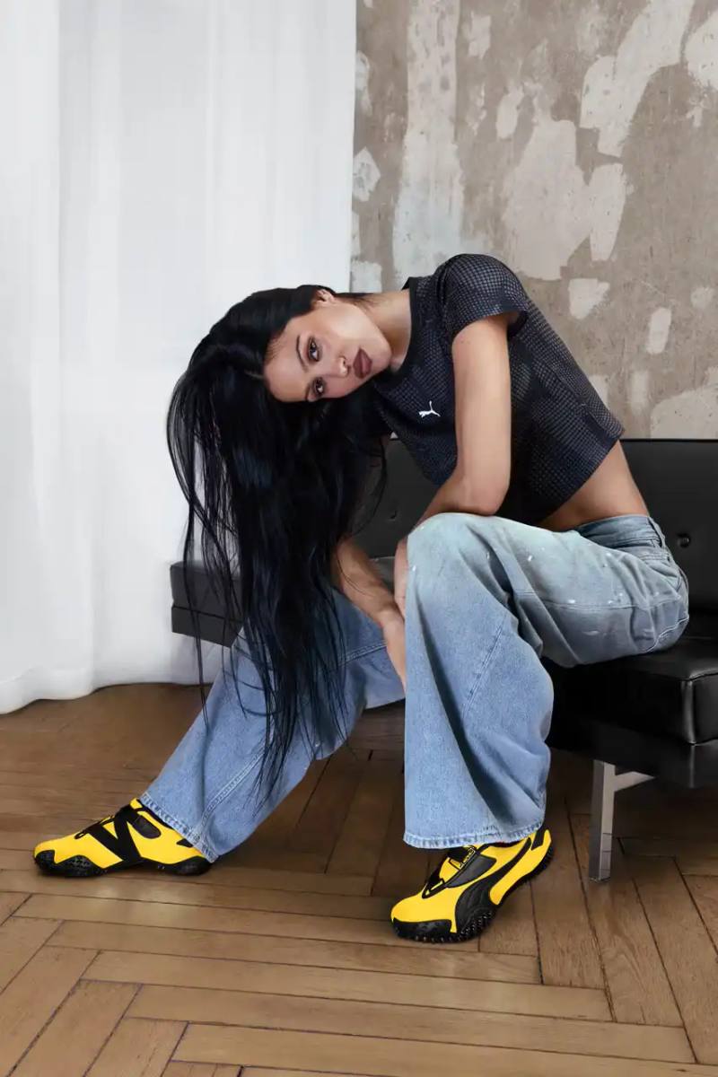 image of PUMA's latest Mostro sneaker release in yellow colorway, featuring model Amelia Gray in promotional campaign imagery. Includes product specifications, pricing at $120 USD, and June 5 release date through PUMA retail channels.