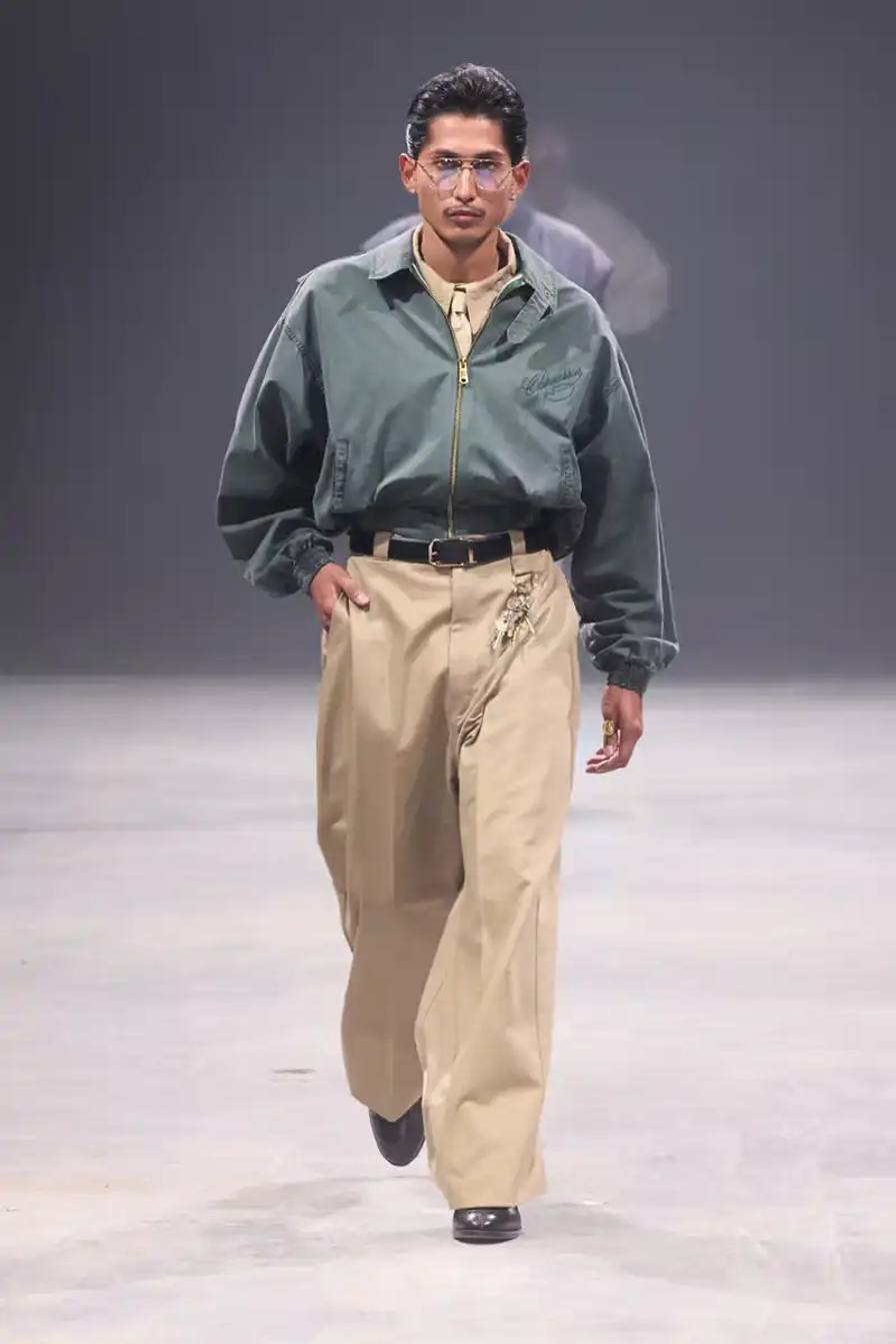 Models walk the runway at Willy Chavarria's SS25 'América' show, wearing dramatic workwear-inspired designs against an industrial backdrop
