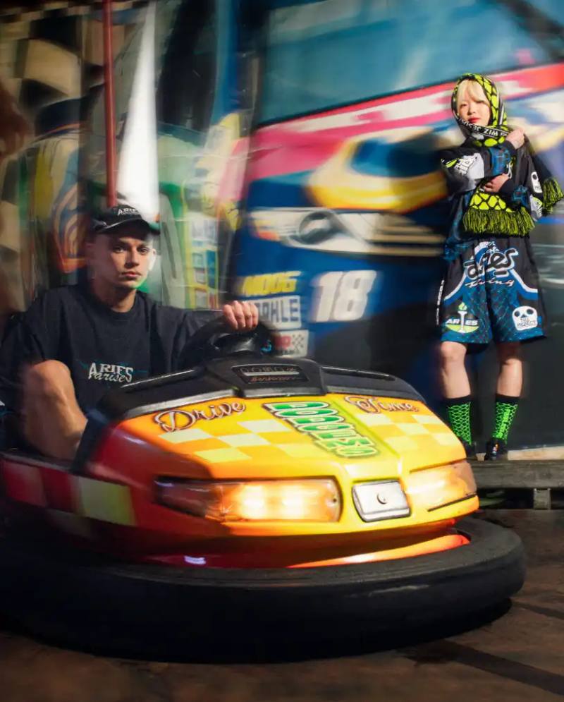 image of the launch of a collaborative fashion collection between retailer END. and streetwear brand Aries. The nine-piece "Arcade" collection draws inspiration from 1990s arcade games and motorsports culture, featuring items like graphic t-shirts, shorts, accessories, and caps with racing-themed designs. The piece includes details about pricing (£35-£170), availability through END.'s online store and physical locations, and the campaign photography shot in an actual arcade setting. The collaboration marks part of END.'s 20th anniversary and represents Aries' first partnership with the retailer.