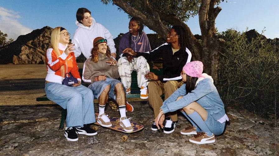 An image shows three people wearing PUMA Suede sneakers and sportswear in an urban street setting with posters on a utility box.