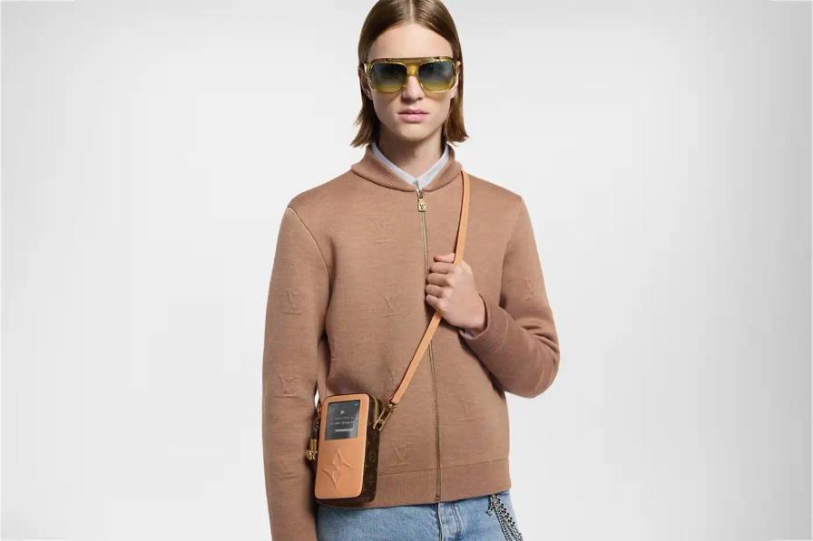Louis Vuitton Spring 2025 accessories collection featuring music technology-inspired luxury items. The image shows an iPod-shaped leather crossbody bag with a display screen showing 'Louis Vuitton Collection Spring 2025' and an LV monogram replacing the scroll wheel. Also visible are a cassette player-styled wallet with embossed control buttons and a cassette tape card holder with 'Side A' and 'Side B' graphics. Gold headphone-shaped zipper pulls complete the nostalgic design.