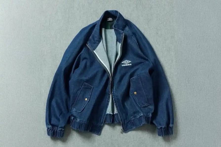 Japanese retailer FREAK'S STORE partners with British sportswear brand UMBRO on a denim blouson jacket featuring a stand collar, minimal branding, and Black Watch tartan interior details, releasing late January 2026.