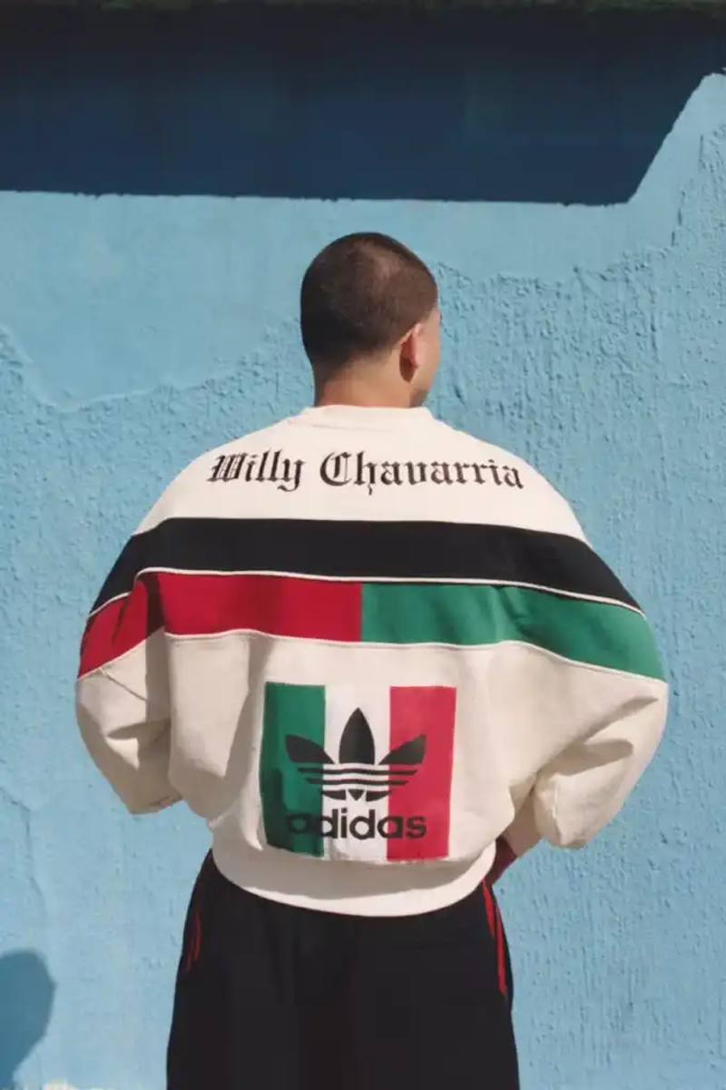 ADIDAS ORIGINALS TEAMS WITH WILLY CHAVARRIA ON CHICANO-INSPIRED COLLECTION image of the Spring/Summer 2025 collaboration between adidas Originals and designer Willy Chavarria. The collection celebrates Chicano culture through fashion, featuring oversized silhouettes and Mexican cultural symbols. Key pieces include tracksuits with Three Stripes, redesigned Trefoil logos with rose embroidery, co-branded hoodies with red and green panels, and the revamped 1978 Jabbar basketball shoe. The collection launches in two drops: May 8 and July 10, available through the CONFIRMED app and select retailers. The campaign was photographed by Carlos Jaramillo in Los Angeles with Chavarria's friends and family.