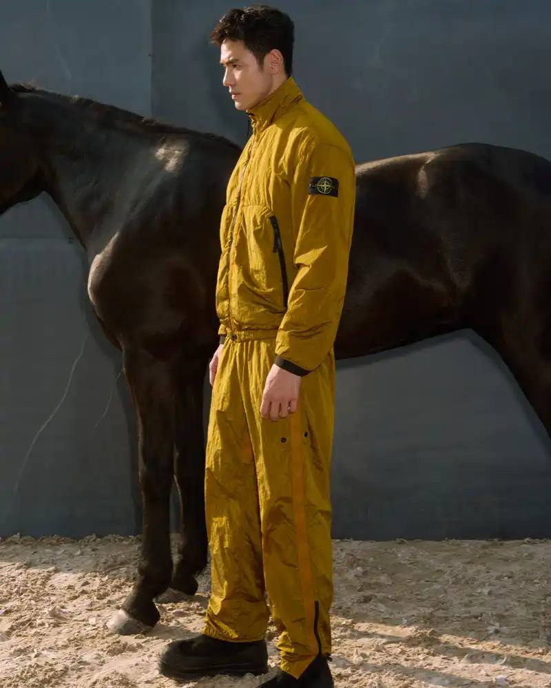 Stone Island introduces a Lunar New Year collection for the Year of the Horse, featuring a stand collar jacket, joggers, cap, and sling bag in NYLON METAL fabric with gold and dark brown colors.