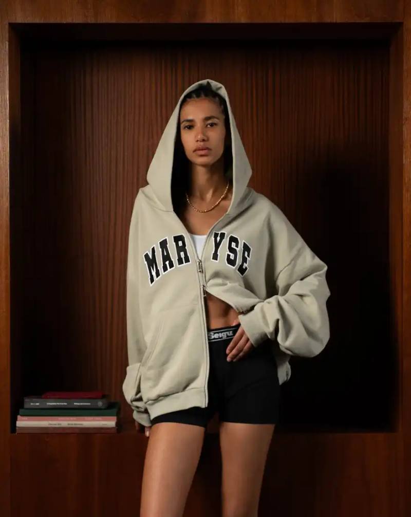image about the launch of Maryse Seigu's third fashion collection "CANGUIO S/S 25," which pays tribute to Marlene Canguio, the first woman from Guadeloupe to compete in the Olympic Games. The piece discusses the 13-item athletic-inspired collection that combines Caribbean cultural heritage with contemporary urban fashion, key pieces named after notable Afro-Caribbean athletes, and details about the brand's visual storytelling approach. The article includes information about a launch event in New York on May 23, 2025, and online availability starting May 29, 2025.