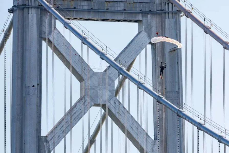 image of Professional skysurfer Sean MacCormac performs historic stunt gliding across San Francisco Bay Bridge cables after helicopter jump, supported by Prada Linea Rossa and Red Bull partnership.