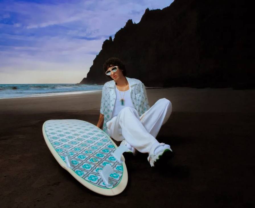 Model relaxing on Tenerife beach at sunset wearing Casablanca Beach Club 2025 gradient monogram linen shirt and trousers