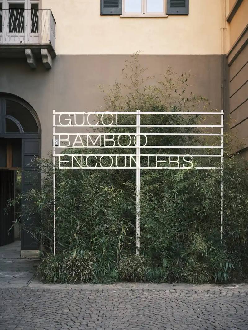 photo of details the "Gucci | Bamboo Encounters" exhibition at Milan's San Simpliciano Cloisters during Fuorisalone 2025. It describes how curator Ippolito Pestellini Laparelli and studio 2050+ have assembled international artists to reimagine bamboo—a material significant to Gucci's design heritage since the 1940s. The text outlines contributions from seven featured artists/collectives, including Anton Alvarez, Dima Srouji, Kite Club, Laurids Gallée, Nathalie Du Pasquier, Sisan Lee, and the back studio. The exhibition runs April 8-13, 2025, with public events scheduled throughout.