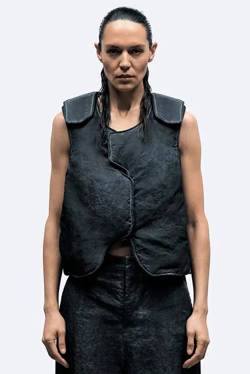pic of A-COLD-WALL*'s Spring/Summer 2025 collection called "Pink Noise," which draws inspiration from British radio culture. The piece describes the collection's technical outerwear, including utility jackets with toggles and drawstrings, ice blue collared jackets paired with loose shirts, color-blocked knitwear in black, brown and cream, graphic t-shirts, ribbed vests, and practical sling bags. The article notes that this collection follows the departure of founder Samuel Ross and the brand's acquisition by Four Marketing. The collection maintains A-COLD-WALL*'s signature gorpcore aesthetic with functional designs and is currently available on the brand's website.